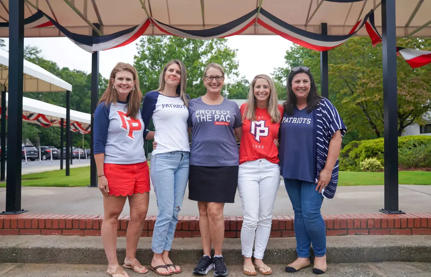 Five women smiling with their arms around each other