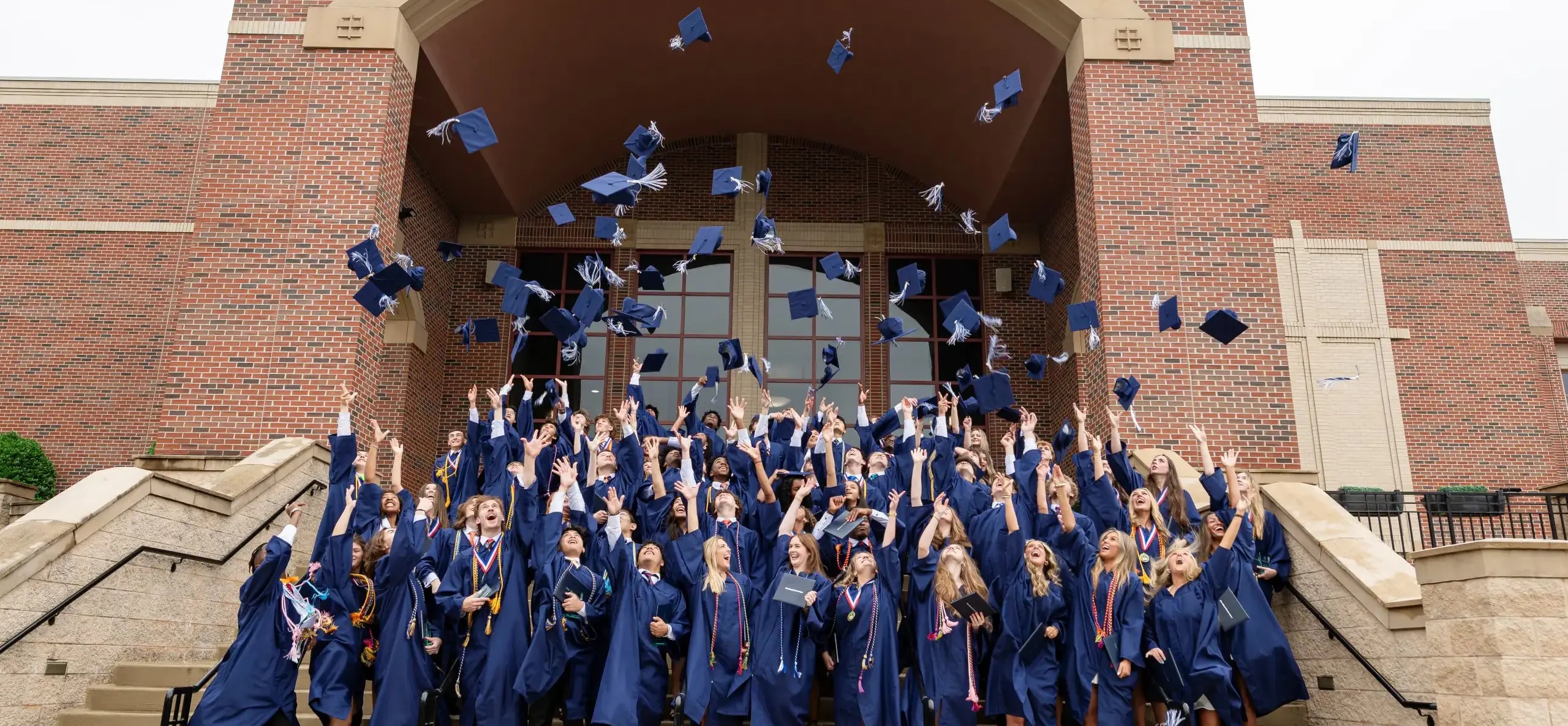 Students tossing graduation gaps in the air, standing on steps