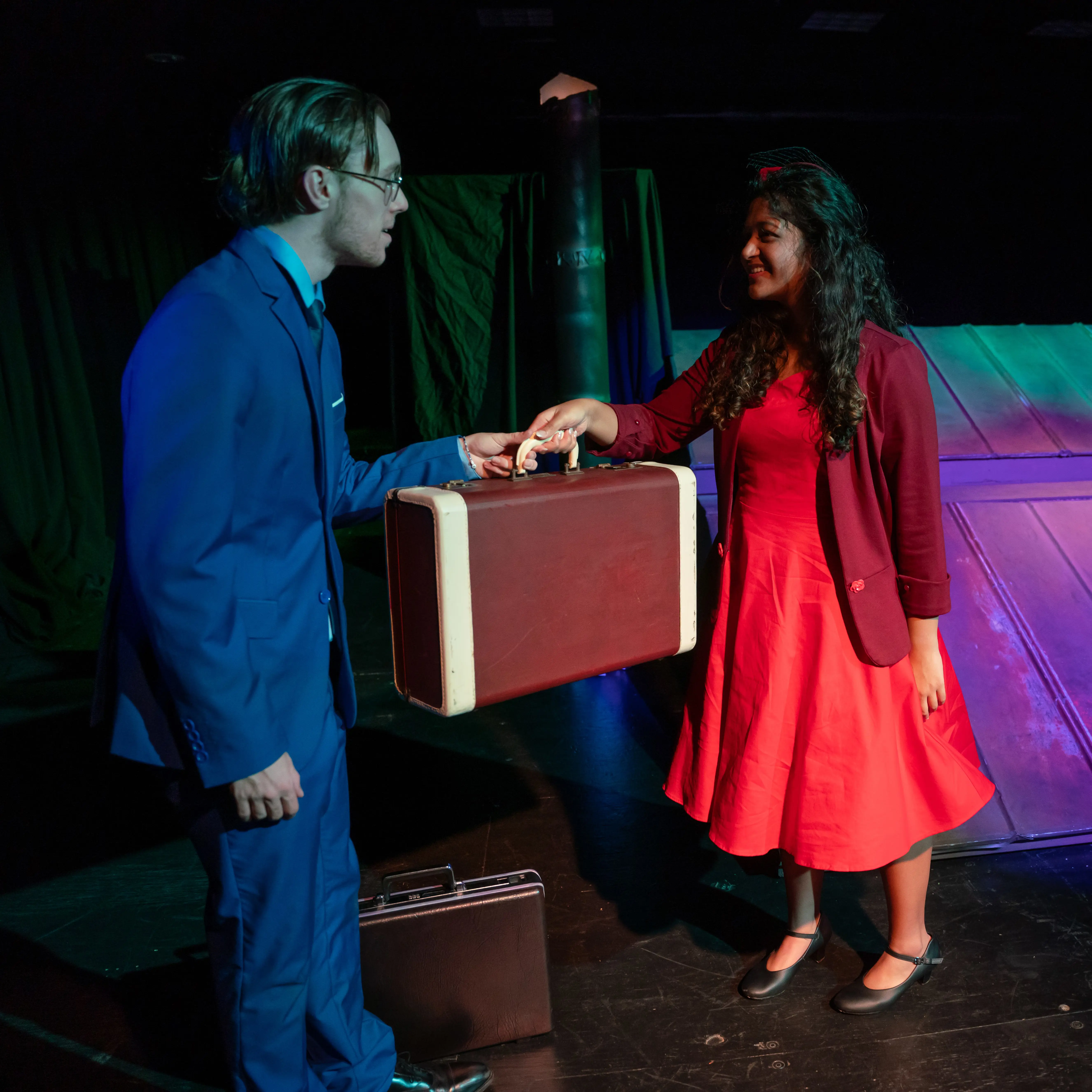 Two students in a play hand a briefcase between each other