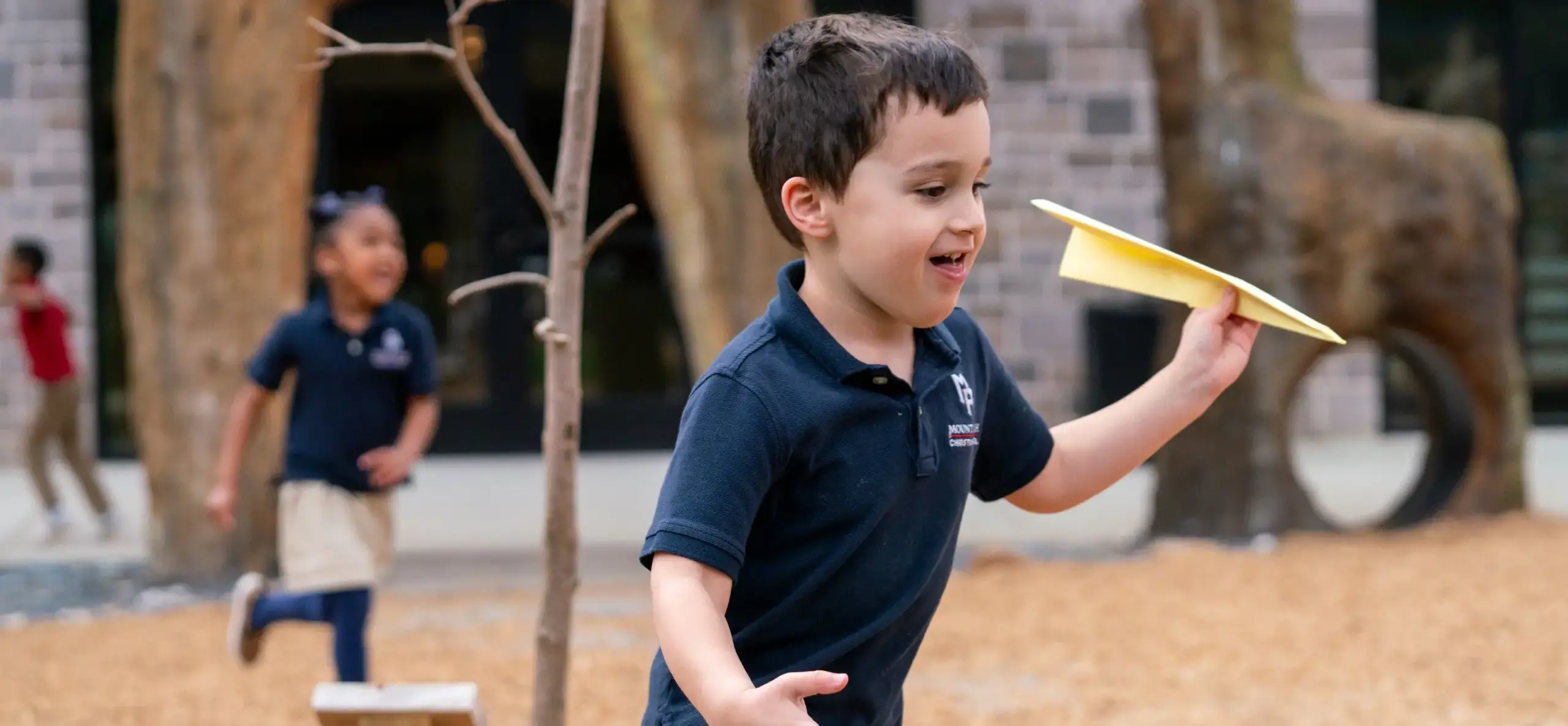 boy runs holding a paper airplane at the playground