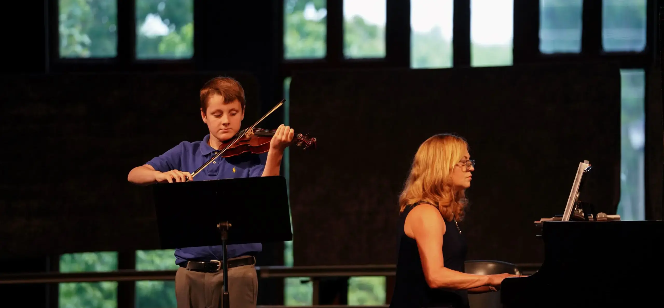 Two students performing onstage, one at the piano and one with a violin