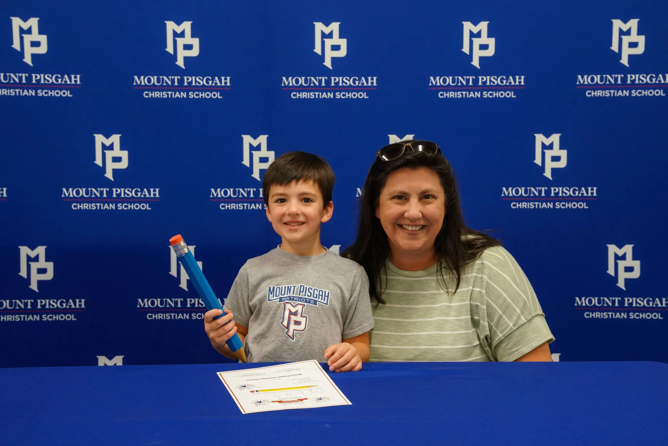 Student and parent at kindergarten signing day. He has a comically large pen.