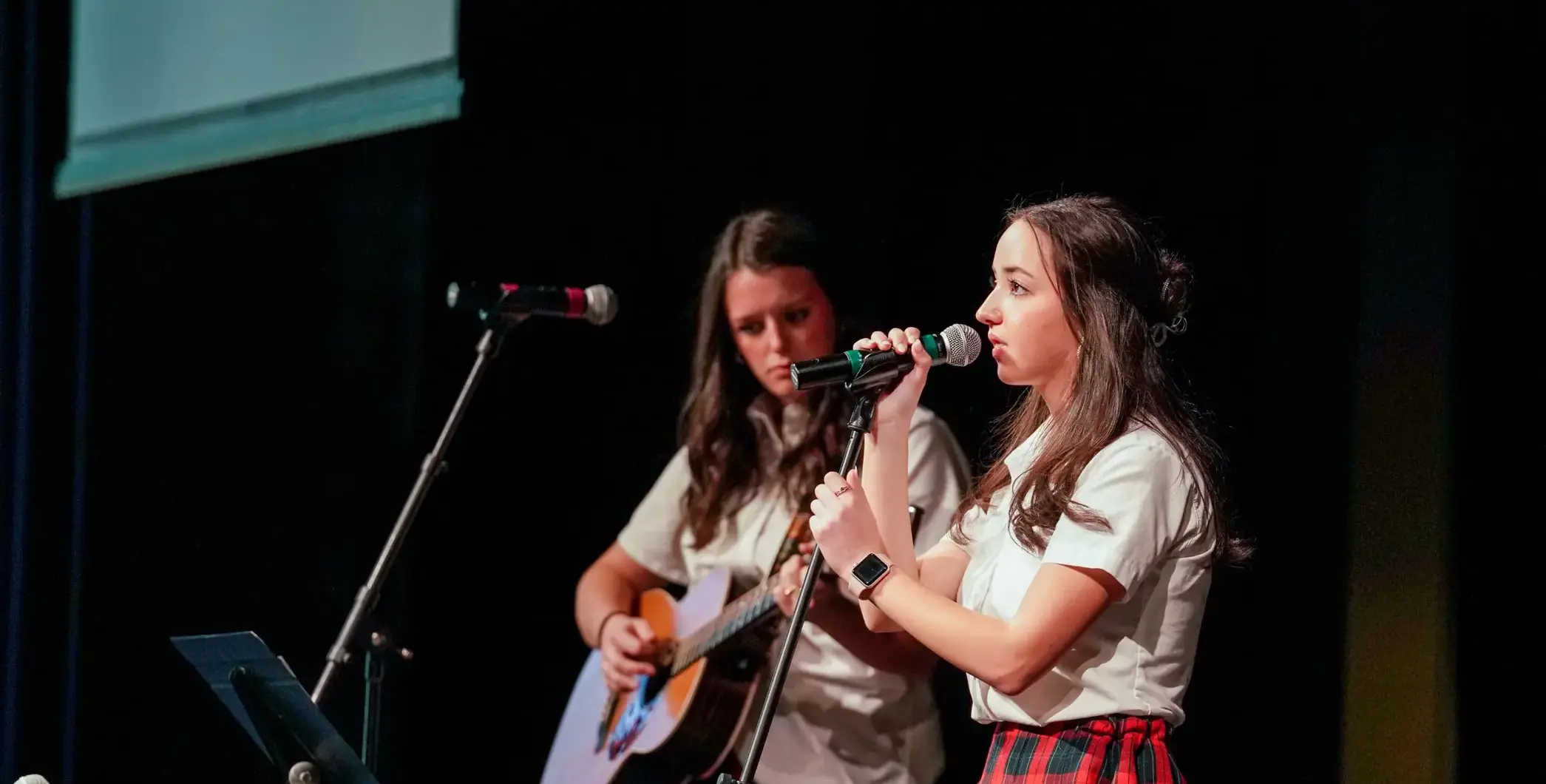 Two students performing onstage, one singing and the other playing guitar
