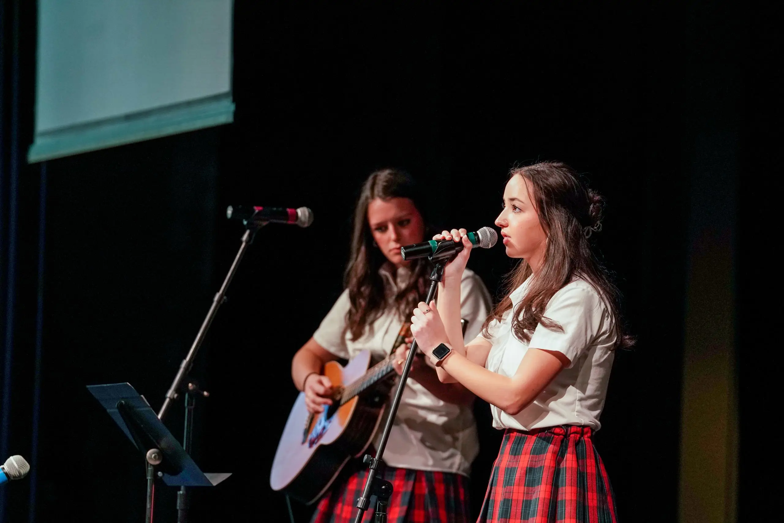 Two students performing onstage, one singing and the other playing guitar